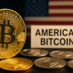 米国旗を背景に「AMERICAN BITCOIN」と書かれた札と金色のビットコインのコインが写る接写写真