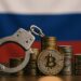 ロシア国旗を背景に、ビットコインと手錠が並ぶ写真。違法仮想通貨取引の取り締まりと押収を象徴。